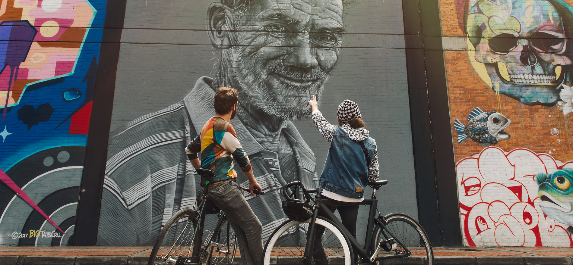 自転車に乗ったカップルが背中合わせでコロンビアのストリート アートの壁画を眺めています。