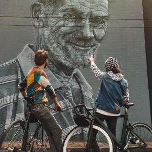 自転車に乗ったカップルが背中合わせでコロンビアのストリート アートの壁画を眺めています。