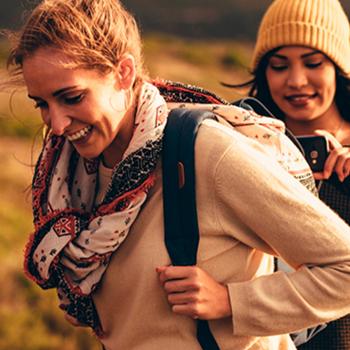 A group of young people walks along a mountain at a sunset.